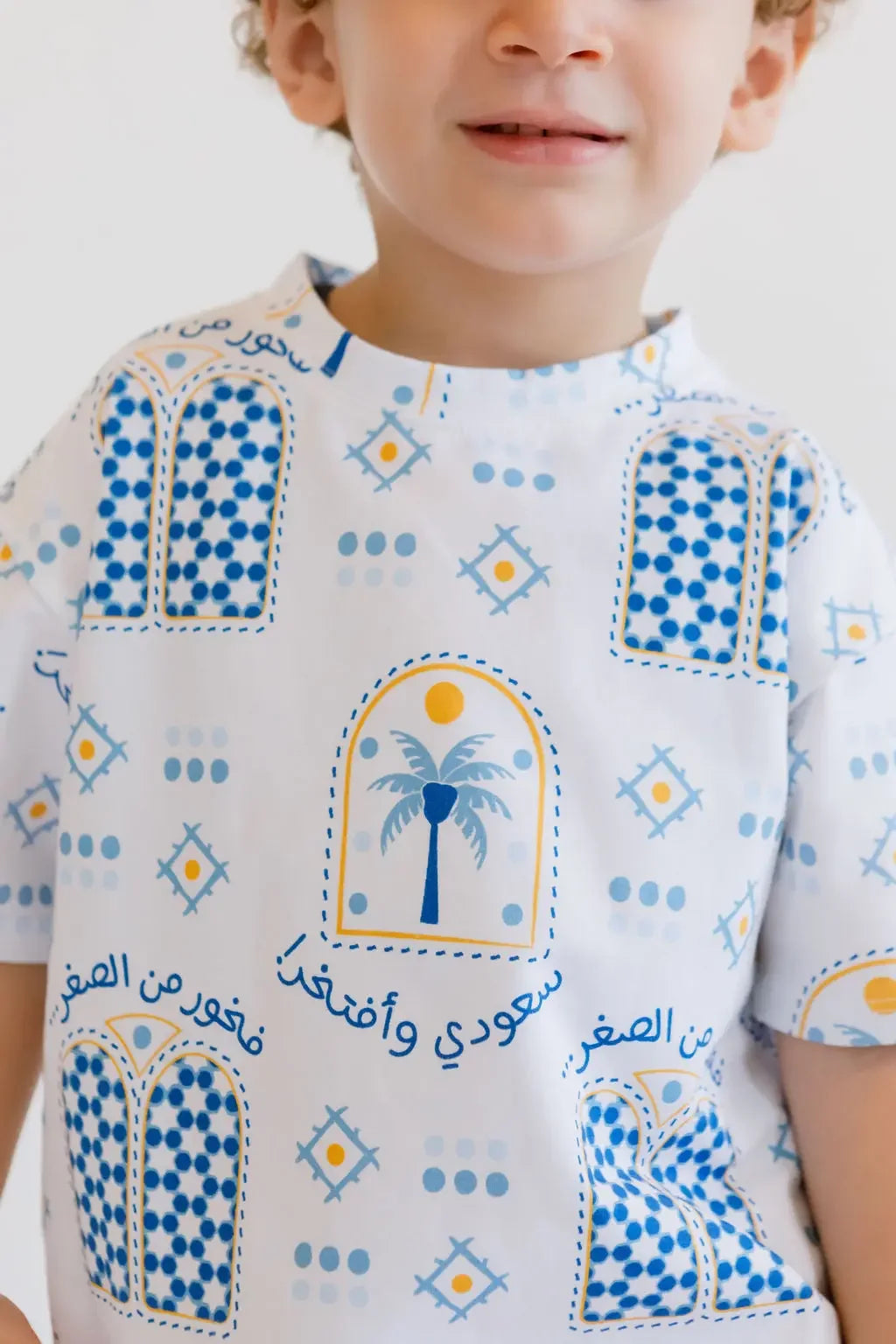 A close-up of a smiling boy wearing our Saudi T-Shirt, featuring the palm and “سعودي وأفتخر” print that celebrates national pride.