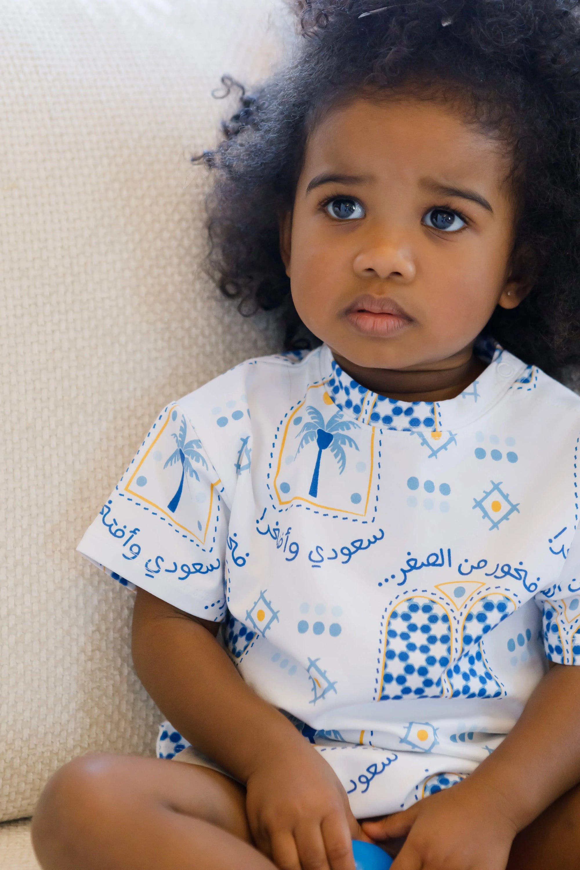 A thoughtful little girl sitting calmly while wearing our Saudi T-Shirt, proudly showcasing the “سعودي وأفتخر” design.
