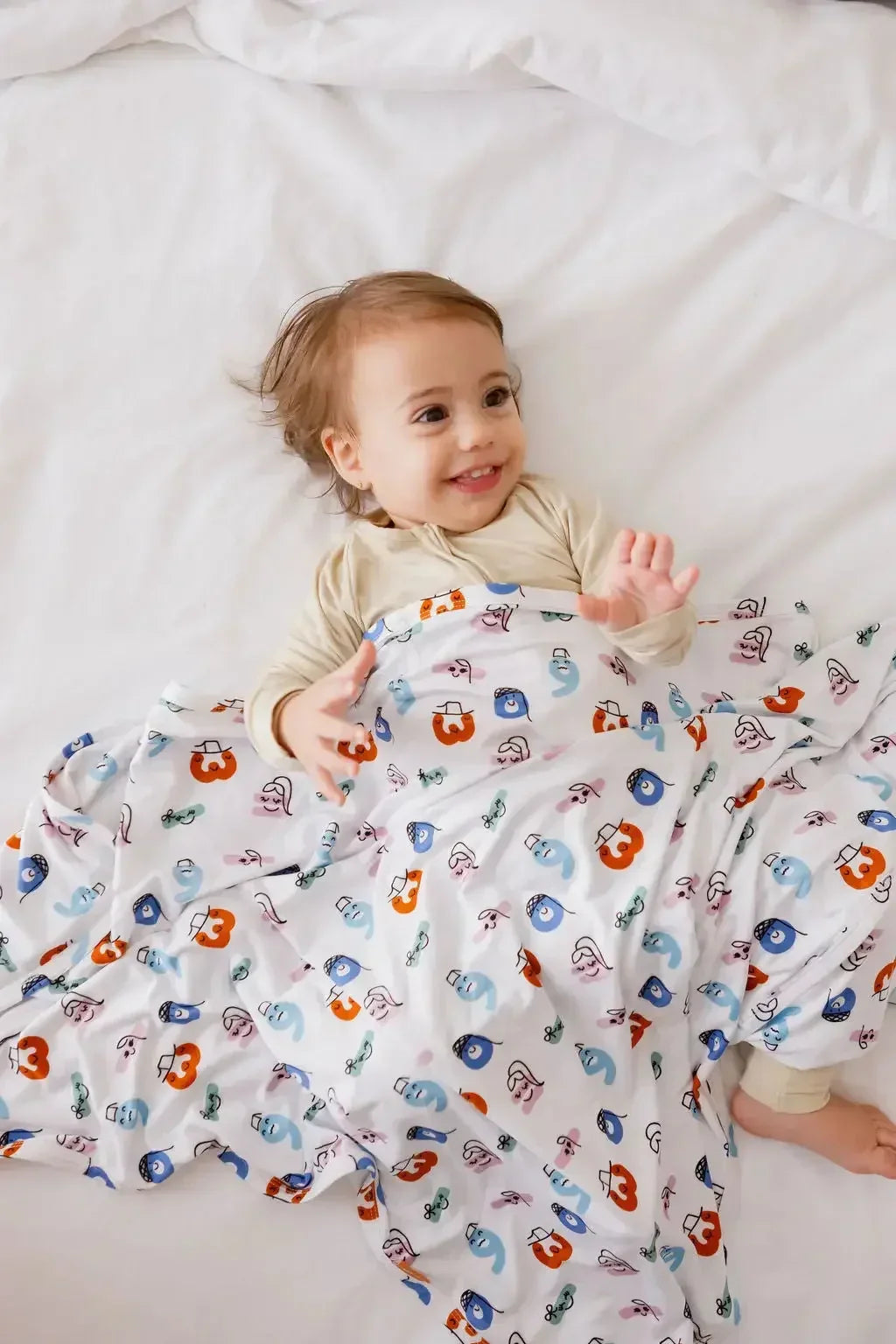 A smiling baby snuggled in our Nohm Tanween Bedding Set, wrapped in the playful comfort of its soft Arabic-inspired design.