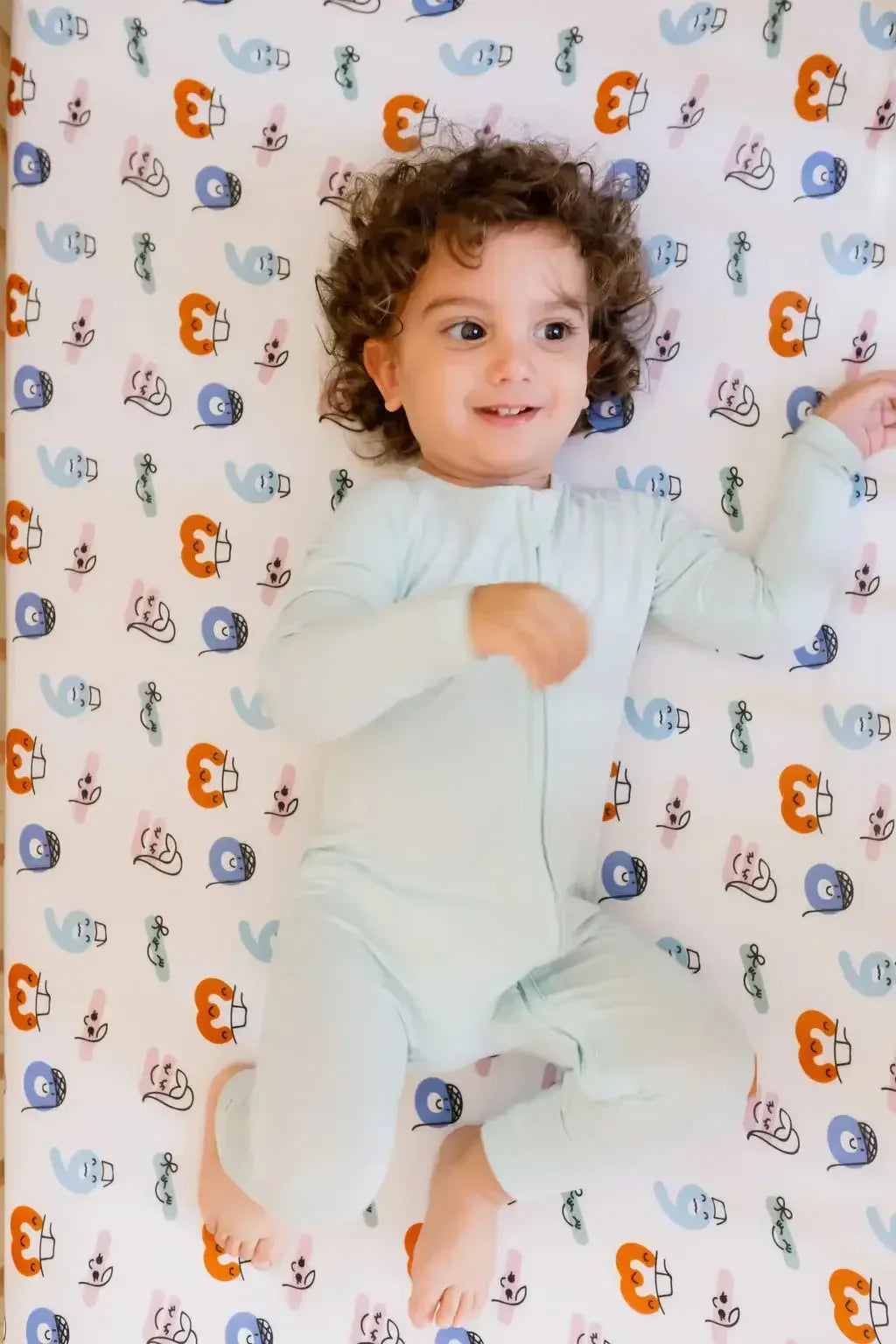 A baby lying on our Nohm Tanween Crib Sheet, enjoying the softness and playful charm of its Arabic-inspired patterns.