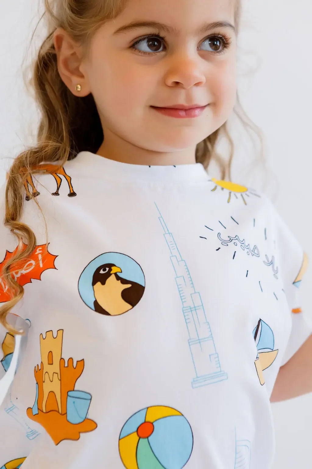 A close-up of a smiling girl wearing our UAE T-Shirt, featuring playful icons that celebrate the nation’s landmarks and culture.