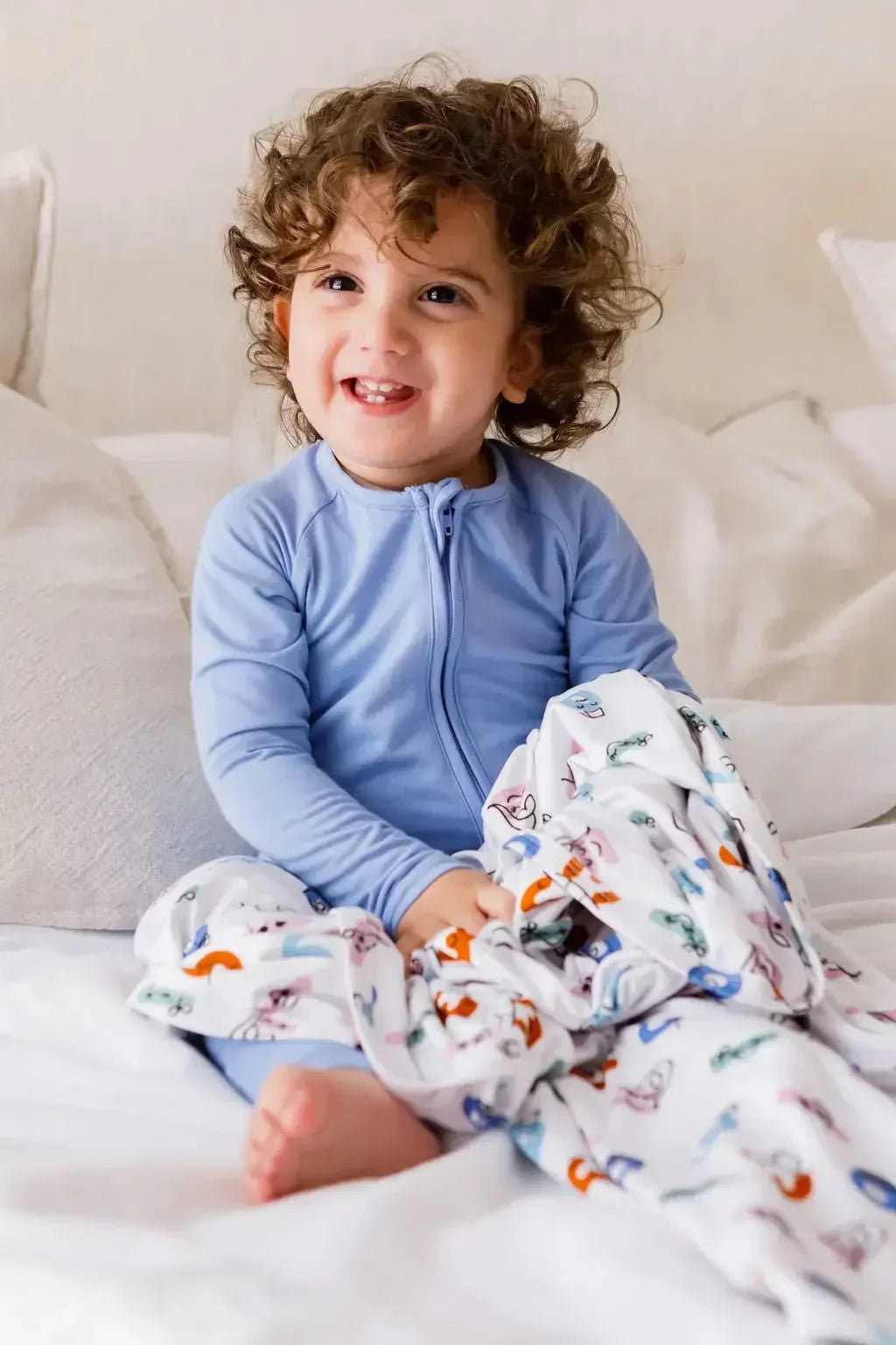 A smiling toddler wearing the **Bahry Pyjama** from the **Watermelon Bundle**, a soft light-blue bamboo one-piece designed for cozy comfort and easy movement.

