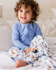 A smiling toddler wearing the **Bahry Pyjama** from the **Watermelon Bundle**, a soft light-blue bamboo one-piece designed for cozy comfort and easy movement.
