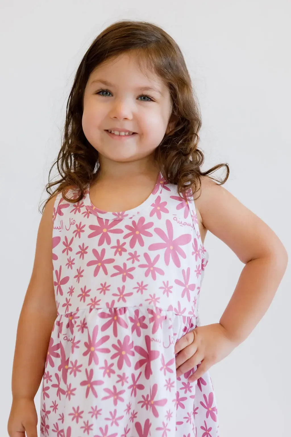 A confident girl smiling brightly while wearing our Yasmine Dress, blooming with pink jasmine flowers for a sweet, summery vibe.