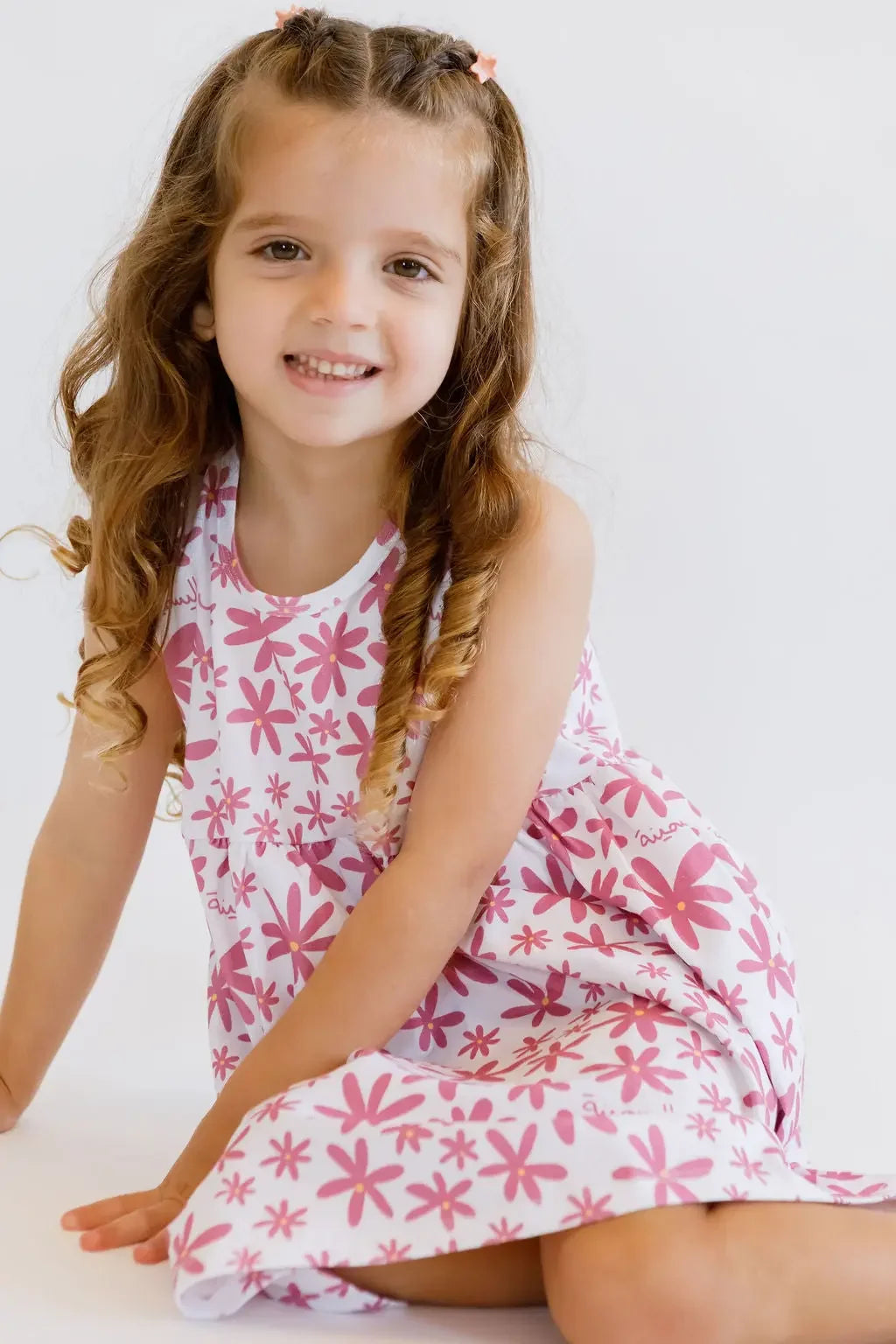 A happy girl sitting gracefully while wearing our Yasmine Dress, covered in soft pink jasmine blooms for a charming, airy look.