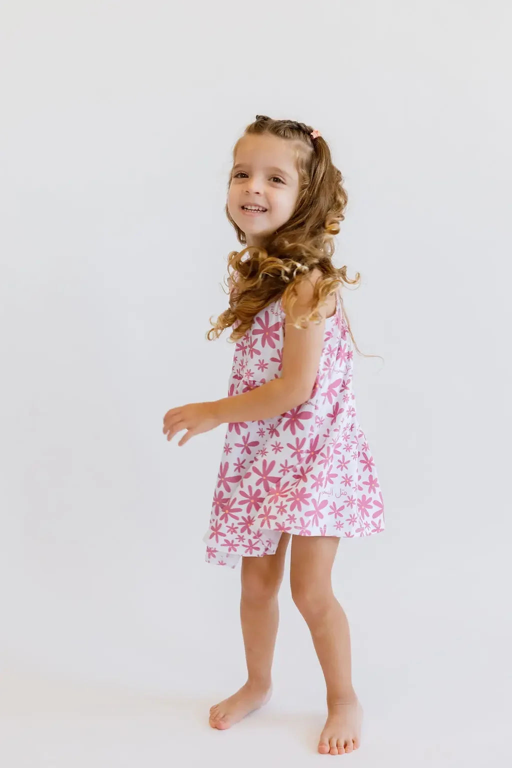 A joyful girl twirling in our Yasmine Dress, featuring a soft pink jasmine flower pattern that captures playful elegance.