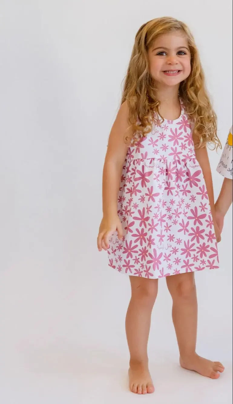 A smiling girl standing happily while wearing our Yasmine Dress, blooming with delicate pink jasmine flower prints.