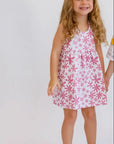 A smiling girl standing happily while wearing our Yasmine Dress, blooming with delicate pink jasmine flower prints.
